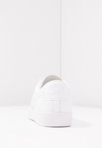 White leather sneaker with a round toe, smooth surface, and tonal stitching. Features embossed Nike logo on the heel tab and a flat rubber sole.