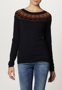 Marineblauer Pullover mit langen Ärmeln, ausgestattet mit einem bunten geometrischen Muster im Schulterbereich in Rost, Gold und Rot. Weiches Strickmaterial, Rundhalsausschnitt.