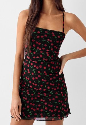 Robe noire à fines bretelles, ornée d'un motif de cerises rouges et de feuilles vertes. Silhouette ajustée avec des fronces à la taille.