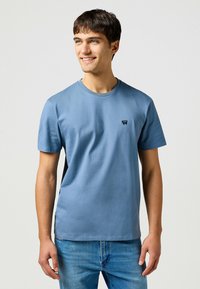 Lichtblauw T-shirt met korte mouwen van katoen, met een ronde hals en een klein logo op de borst. Gemaakt met blauwe jeans.