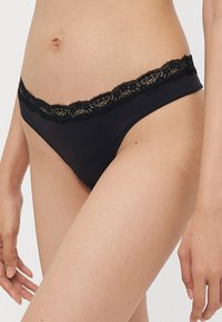 Bas de bikini noir avec une délicate bordure en dentelle au niveau de la taille. Tissu doux et couverture minimale avec une texture lisse.