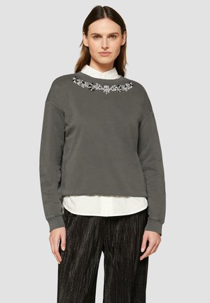 Grijze cropped sweatshirt met floral kralenversiering bij de hals, gecombineerd met zwarte textuurplooibroek en een witte overhemd met kraag.