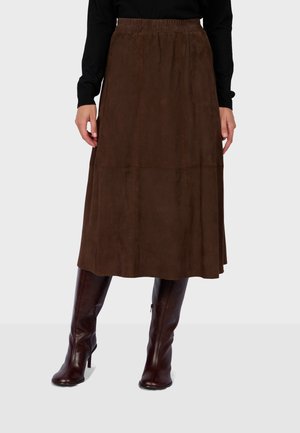 Donna che indossa una gonna midi marrone con vita elastica abbinata a stivali marrone scuro al ginocchio con tacco e una maglia nera a maniche lunghe.