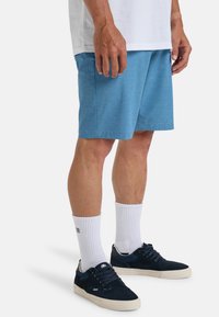 Lichtblauwe sportieve shorts met een rechte snit, gecombineerd met witte crew-sokken en marineblauwe sneakers met een tankleurige zool en accenten.