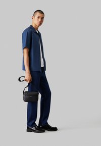 Camicia a maniche corte blu marina, canottiera bianca, jeans in denim scuro, borsa nera con tracolla e scarpe nere eleganti con finitura testurizzata.