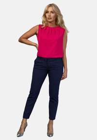 Fuksjowa bluzka bez rękawów z plisowanym dekoltem, zestawiona z ciemnogranatowymi spodniami w wzory oraz obcasami w wężowy wzór.