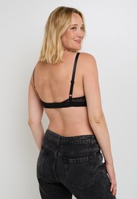 Reggiseno in pizzo nero con spalline regolabili, chiusura con gancetto sul retro, caratterizzato da una texture morbida. Abbinato a jeans in denim scuro a vita alta.