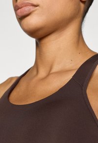 Hnedý tielkový top so hladkou textúrou, výstrihom do U a širokými ramienkami, zdôrazňujúci priliehavý strih.