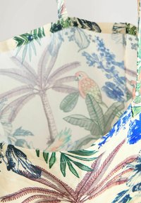 Genanvendelig tote taske lavet af stof, der har et tropisk blomstermotiv og fugleprint i livlige farver. Indersiden har en lys baggrund.
