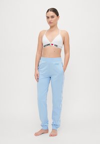 Fehér bralette fekete és piros felirattal, kék sportnadrággal, oldalsó logóval. Puha anyag, laza szabás, egyenes szárú dizájn és rugalmas derékpánt.