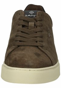 Braune Wildleder-Sneaker mit runder Spitze, flacher cremefarbener Sohle und passenden Schnürsenkeln. Sie verfügen über eine glatte Textur und eine minimale Markenkennzeichnung auf der Zunge.