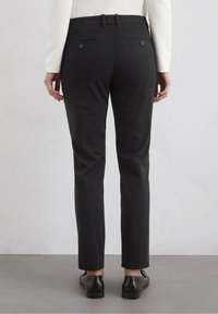 Black trousers with a straight cut, two back pockets with buttons, and a belt looped waistband. Material appears smooth and even textured.