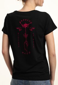 Sort bomulds T-shirt med rød grafik, der viser en hånd, der holder en blomst, omgivet af teksten "growing wild mistress of evil." Korte ærmer.