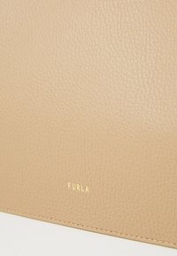 Bēša ādas maks ar strukturētu virsmu, kas rotāts ar pārlieku smalku zelta "FURLA" logotipu un kārtīgi izšūtām malām.