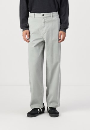 Light gray straight-leg trousers with a button closure, side pockets, and a smooth texture, paired with black sneakers featuring white stripes.