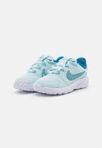 Lyseblå idrettssko med teksturert overdel, hvit såle og turkise detaljer. Har snøringsdesign og kontrasterende Nike-logotype.