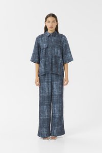 Denim dvodelni komplet z ohlapno, teksturirano modro srajco z dvema žepoma na prsih in širokimi usklajenimi hlačami.