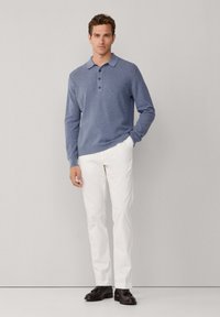 Polo azul de manga larga con una textura suave, tapeta con tres botones y cuello clásico, combinado con pantalones blancos de pierna recta y zapatos de vestir.