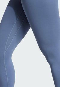 Blauwe sportleggingen van een gladde, elastische stof met een platlocknaad. Het ontwerp heeft een nauwsluitende pasvorm en een matte afwerking.