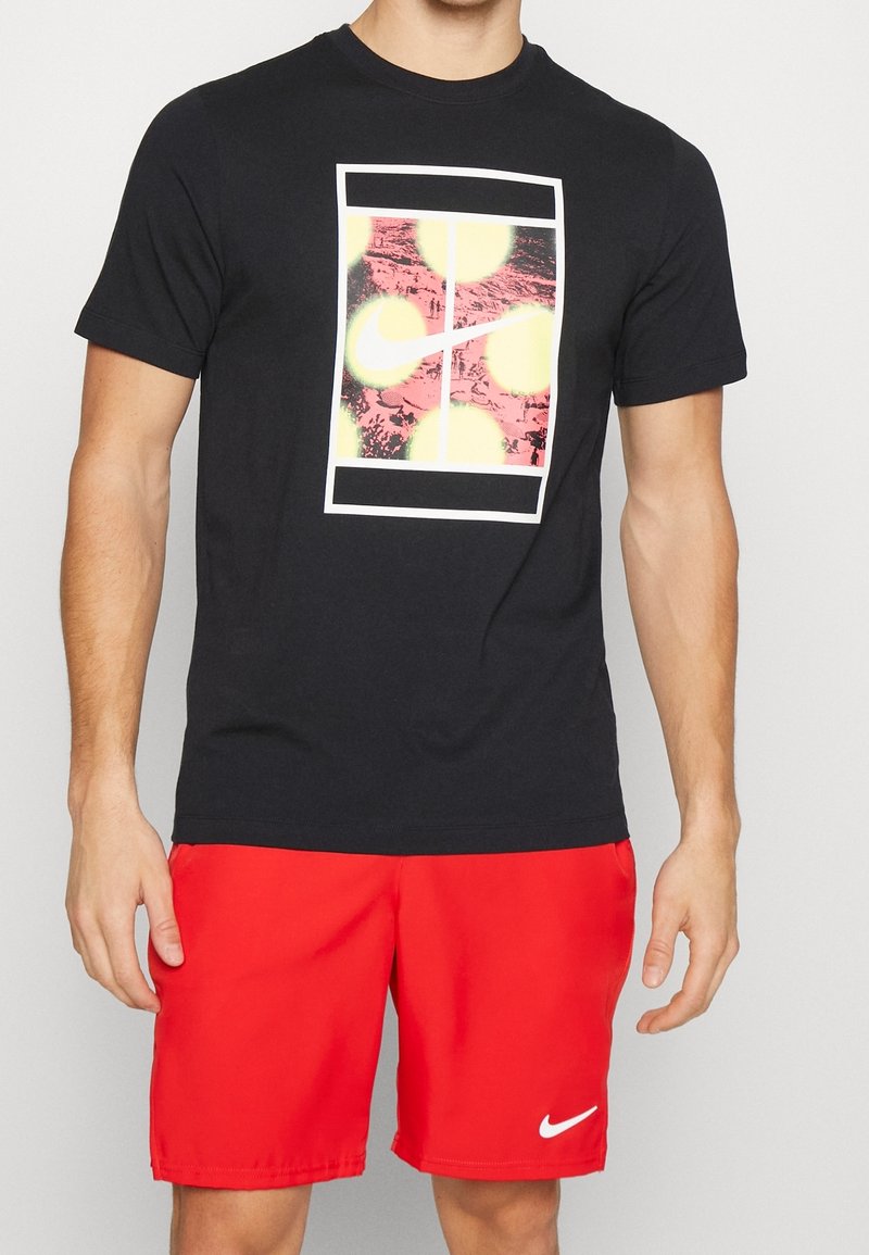 Camiseta de algodón negra con un estampado gráfico de formas circulares amarillas y rosas, con contorno blanco, combinada con pantalones cortos rojos y un logo blanco.