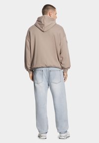 Szara, oversize bluza z kapturem z możliwością regulacji, w połączeniu z jasnoniebieskimi dżinsami. Miękka tekstura, luźny krój z widocznymi detalami szwów.