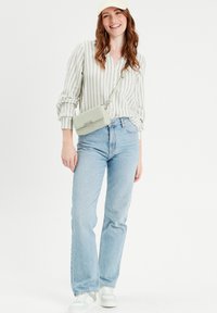 Chemise à rayures vert clair, jean taille haute bleu clair et sac bandoulière vert menthe ; baskets blanches avec des accents verts.