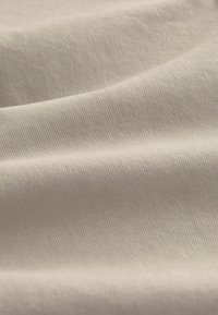 Cotton fabric in a light beige color features diagonal ribbing texture with soft folds, highlighting its smooth surface and subtle sheen.