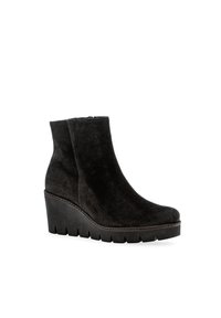 Bottine en suède noir avec un talon compensé, bout arrondi et surface texturée. Elle dispose d'une fermeture éclair sur le côté et de coutures renforcées le long de la semelle.