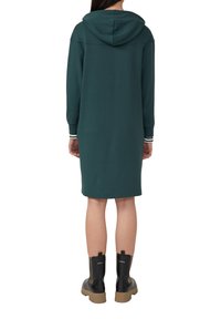 Teal kleurige hoodie jurk met lange mouwen en gestreepte manchetten, gecombineerd met zwarte enkelboots. Glad materiaal en relaxte pasvorm.