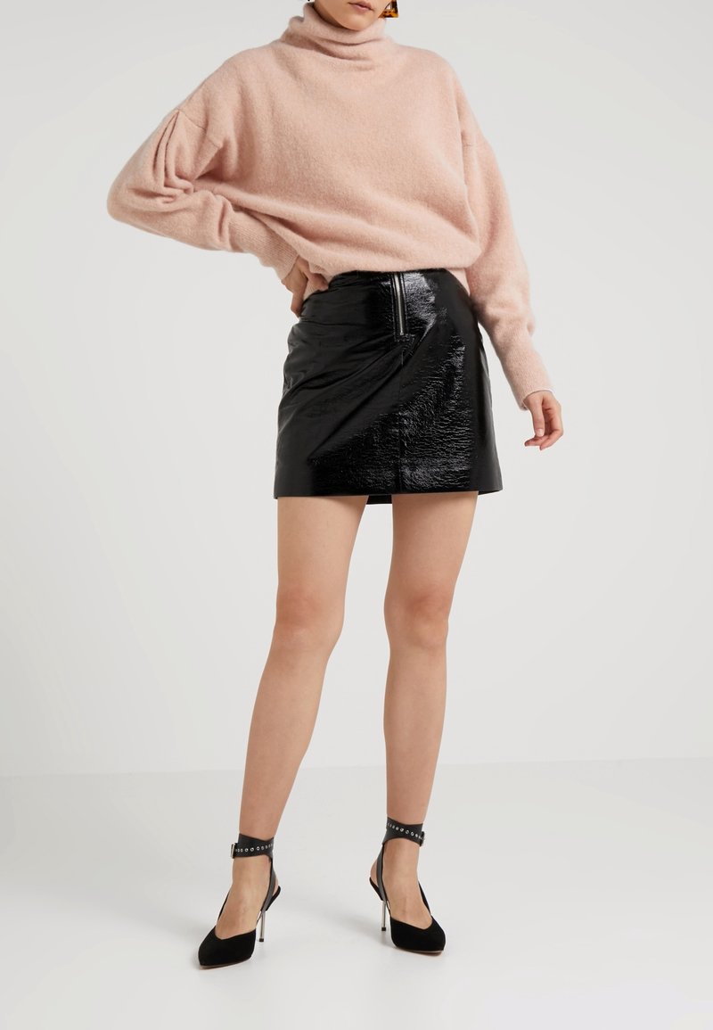 Un pull rose clair à col roulé surdimensionné associé à une mini-jupe en simili cuir noir brillant. Des talons noirs avec des brides à la cheville.