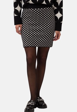 Mini-jupe à motifs noir et blanc associée à des collants noirs transparents et des mocassins noirs avec un détail chaîne argentée.