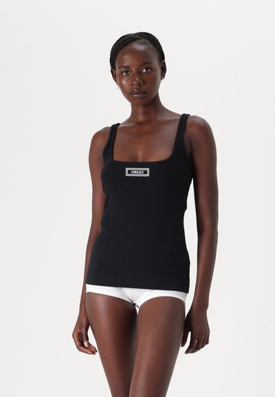 Sort tanktop med firkantet udskæring, tykke stropper og et Versace-logo. Stoffet ser glat og tætsiddende ud. Hvidt undertøj er synligt.