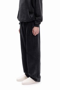 Sudadera negra de gran tamaño con bolsillo frontal, combinada con pantalones de chándal negros de corte holgado con detalles texturizados en forma de "F". Se lleva con zapatos blancos.