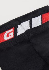 Czarne skarpetki z czerwono-białą-czarną paskowaną opaską na górze, z rozpoznawalnym logo i teksturowanym materiałem dla lepszego chwytu.