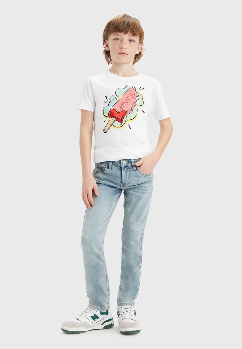 Camiseta de algodón blanca con un gráfico colorido de helado, combinada con jeans azul claro y zapatillas blancas con detalles verdes.