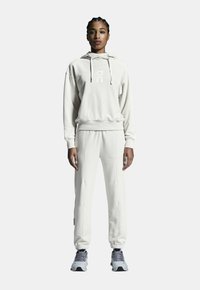 Hoodie beige clair avec logo sur le devant, associé à un pantalon de jogging assorti. Tissu en mélange de coton, coupe décontractée, taille élastique et poignets élastiques.