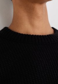 Czarny dziergany sweter z prążkowanym okrągłym dekoltem i teksturowaną tkaniną, przedstawiający zbliżenie kołnierza i okolicy szyi.