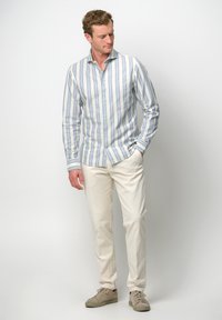 Camicia a maniche lunghe a righe in azzurro chiaro e bianco, con colletto button-down, abbinata a pantaloni beige e sneakers chiare. Tessuto morbido e casual.