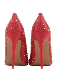 Tacchi alti in pelle rossa con borchie in metallo dorato, punta affusolata e tacco a stiletto con suola beige. Texture liscia e design elegante.