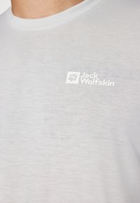 Hellgraues T-Shirt aus weichem Stoff, mit Rundhalsausschnitt und einem kleinen weißen "Jack Wolfskin"-Logo auf der oberen linken Seite.