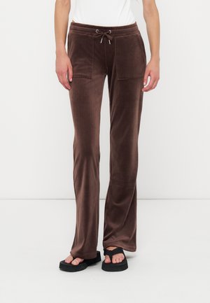 Personne portant un pantalon en velours marron à cordon de serrage avec poches plaquées, un haut blanc et des sandales à plateforme noires, debout devant un fond uni.