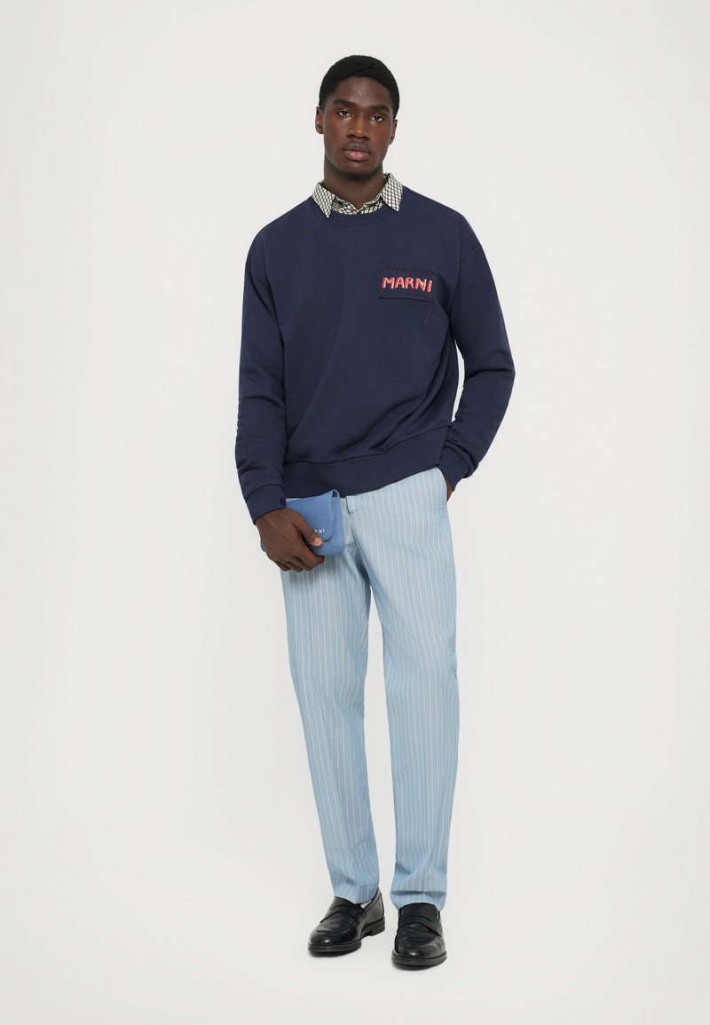 Navy sweatshirt with red "Marni" logo, light blue pinstriped trousers, black loafers, and a small blue pouch. Layered checkered shirt underneath.