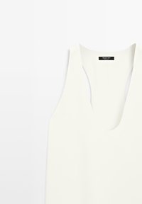 Haut blanc sans manches avec col en V au design simple, montrant l'étiquette au niveau du cou "Massimo Dutti" sur un fond uni.