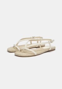 Vita vävda sandaler med platta jutesulor, med flera korsande remmar och ett justerbart ankelspenne för en säker passform.
