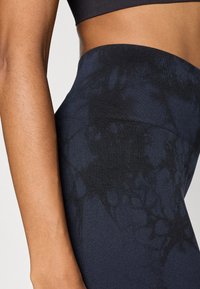 Kõrge vöökohaga retuusid, mis on valmistatud venivast kangast, sügav tumesinine värv ja peen musta lipsuvärvusega muster ning sile vöökoht.