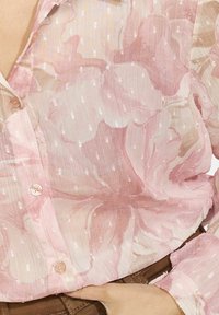Permatomas blusas švelniai rožinės spalvos su gėlių raštu, tekstūruota pakeltomis taškeliais. Turi mygtukų užsegimą ir laisvai krentančią, lengvą medžiagą.