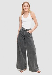 Jeans de denim gris de pierna ancha y cintura alta con un acabado desgastado. Acompañados de una camiseta ajustada blanca y sandalias de color claro.