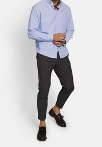 Lichtblauw overhemdd-blouse met een kraag, grijs gestreepte broek, en zwarte instappers met kwastjes. Bevat een enkele borstzak.