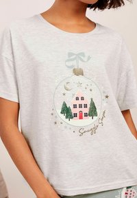 Šedé tričko s krátkým rukávem s ilustrací růžového domu s červenými dveřmi a stromy uvnitř dekorativního ornamentu se zlatými akcenty.