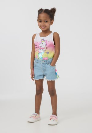 Top minerale bianco con gradiente arcobaleno e grafica di unicorno, abbinato a pantaloni di jeans con orlo sfilacciato, più sneakers pastello.